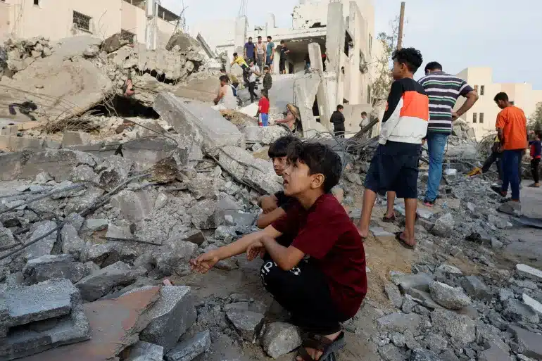 Palestinian children sit amid rubble as others search a building destroyed by Israeli air raids in Khan Younis in the southern Gaza Strip [Mohammed Salem/Reuters]