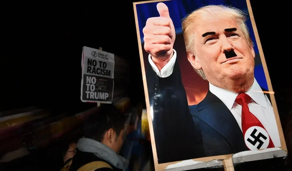 Protest at US Embassy in London, 2016: Demonstrator holds placard depicting Trump with a swastika and Hitler-style mustache [Image via Getty Images].