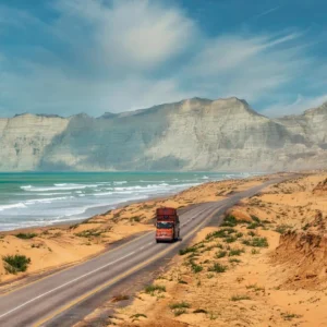 Truck traveling along the Makran Coastal Highway in Balochistan, with rugged cliffs and the Arabian Sea coastline in the background [Image via Getty Images].