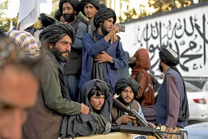 Group of Taliban fighters in Kabul gathered near a wall with their banner flag, holding security positions.