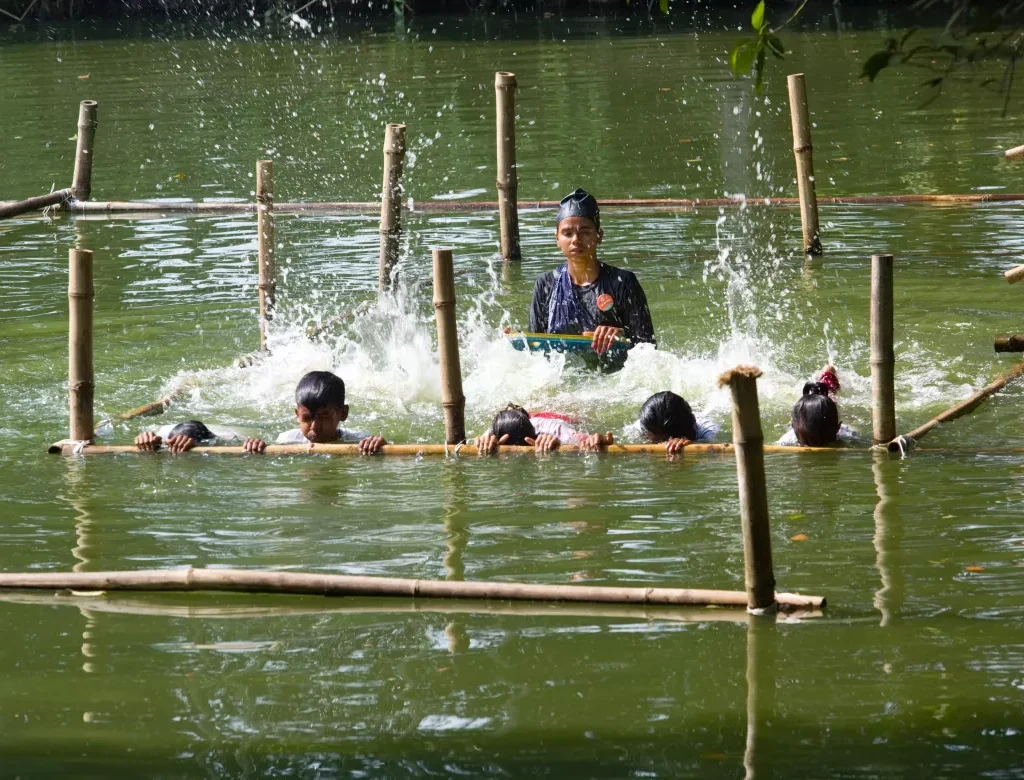 Mim Akter, a prominent young Bangladeshi community swimming instructor, in water with her students, showing them breathing, floating, and rescuing techniques. [Image Credits: UNICEF Bangladesh].