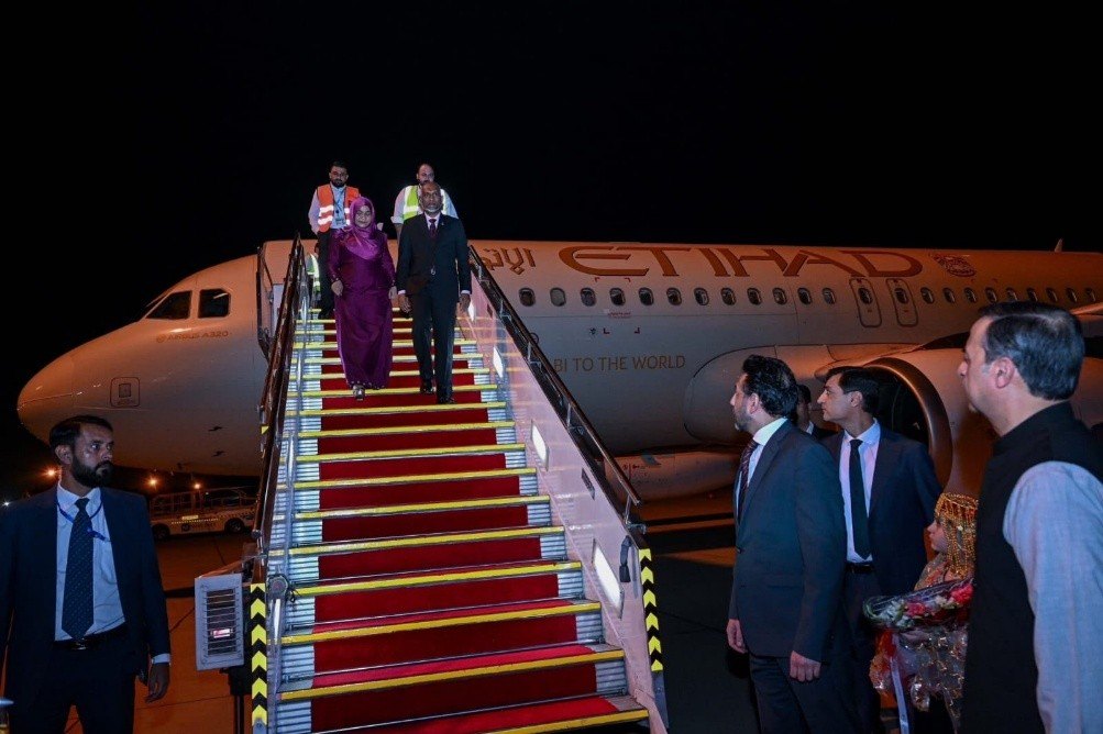 The Maldivian President and First Lady descend the aircraft steps onto a red carpet at night as Pakistani officials wait to greet them.