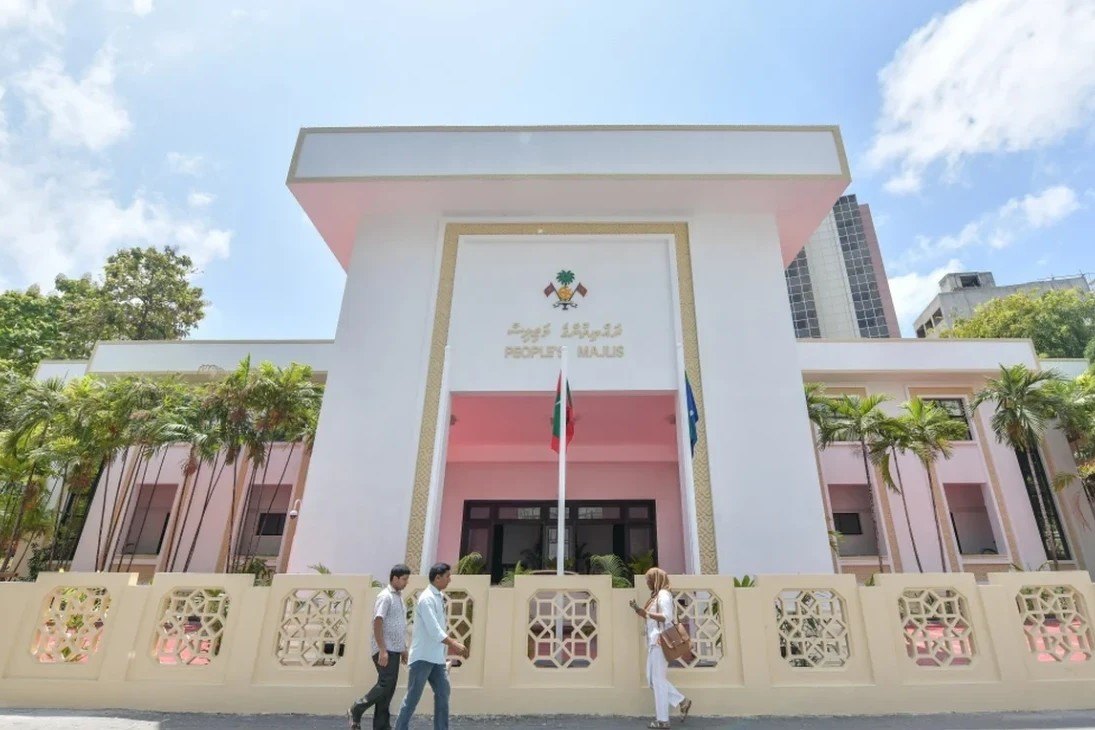 The white facade of the People's Majlis building in Malé, framed by palm trees.