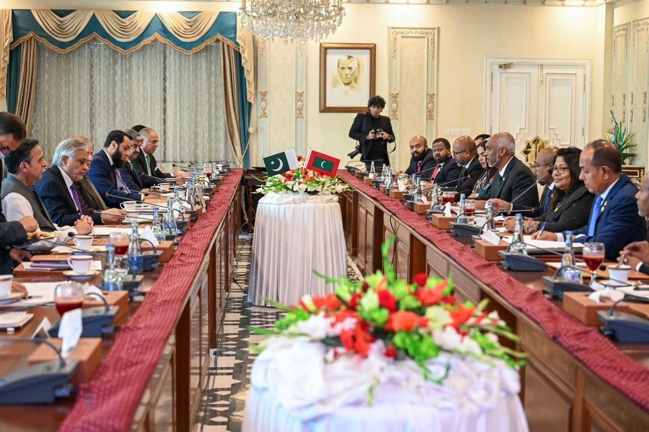 The two delegations face each other across a long conference table decorated with flowers and both national flags.