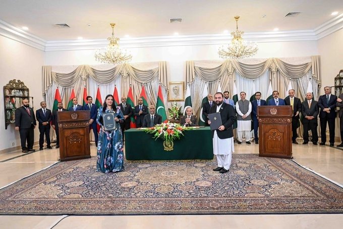 Two officials hold up signed memoranda as the two leaders sit at the table behind them.